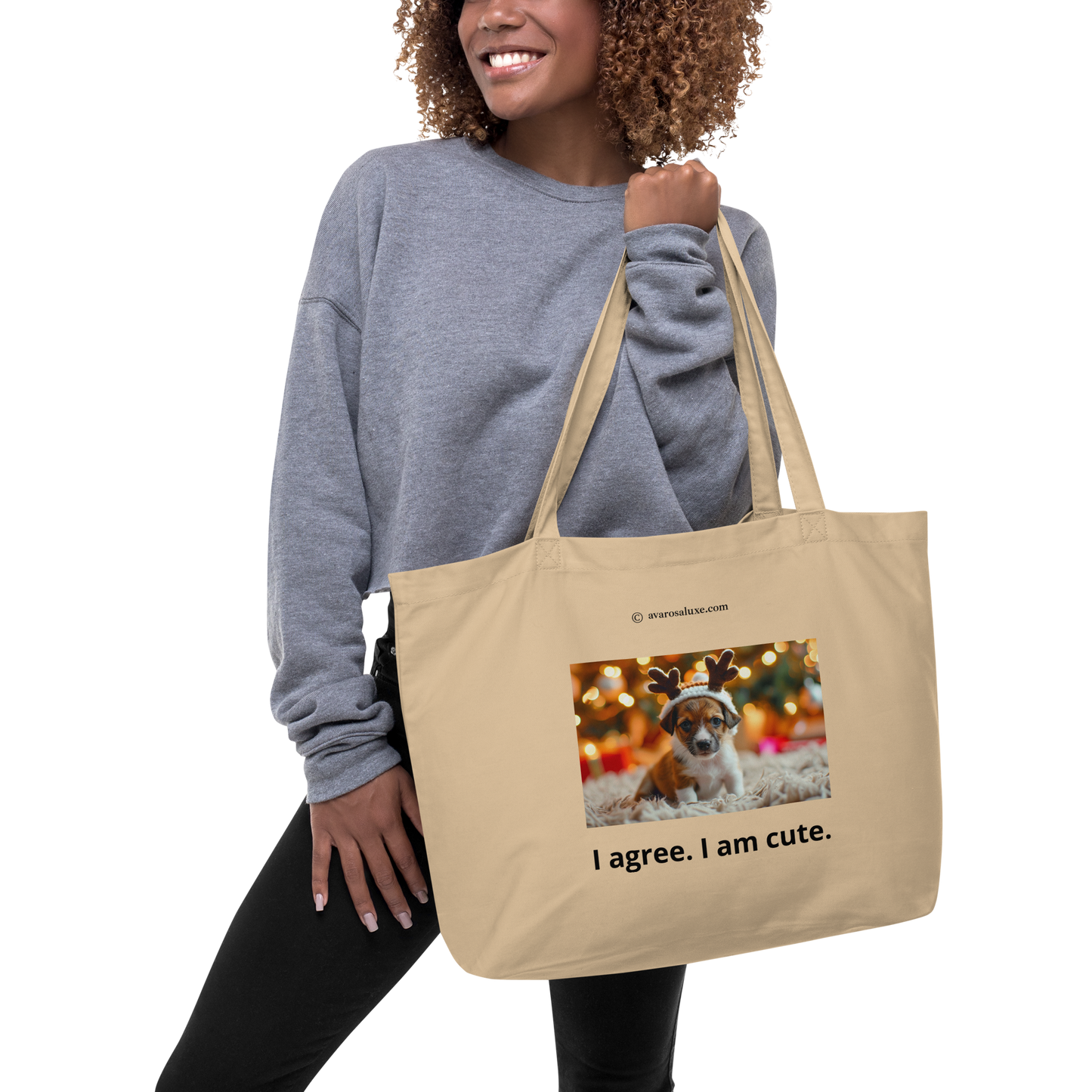 Woman holding a beige tote bag with a printed dog photo and text. Christmas lights in background