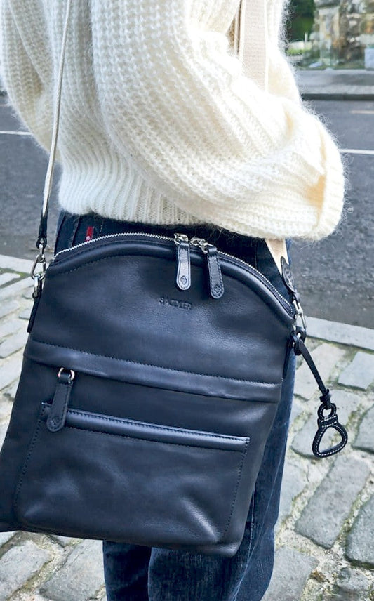 Kimberley handcrafted black leather crossbody bag worn over the shoulder. Woman standing on a street.