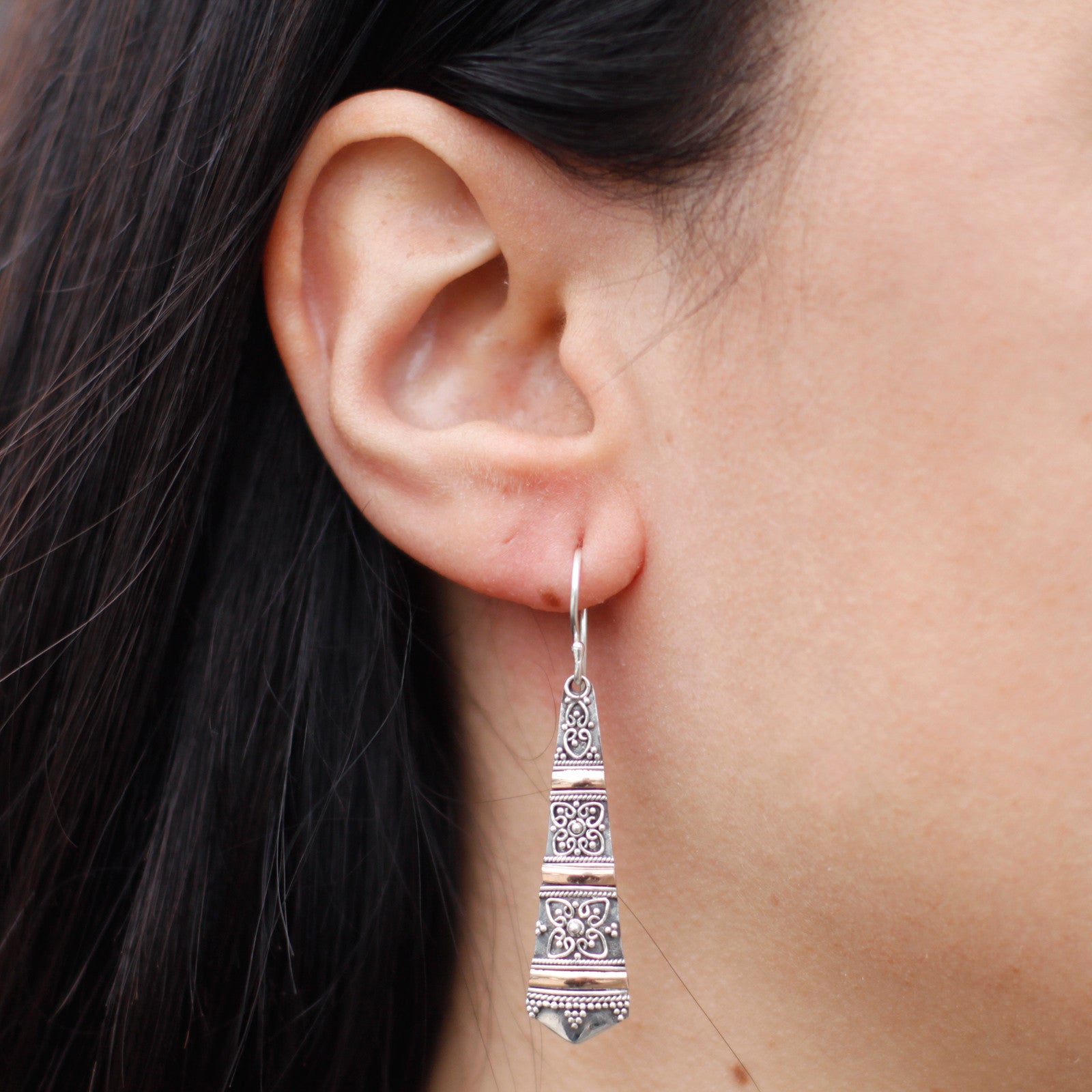 A drop earring shown in a woman's ear. Handmade by artisans. Sterling silver and gold.
