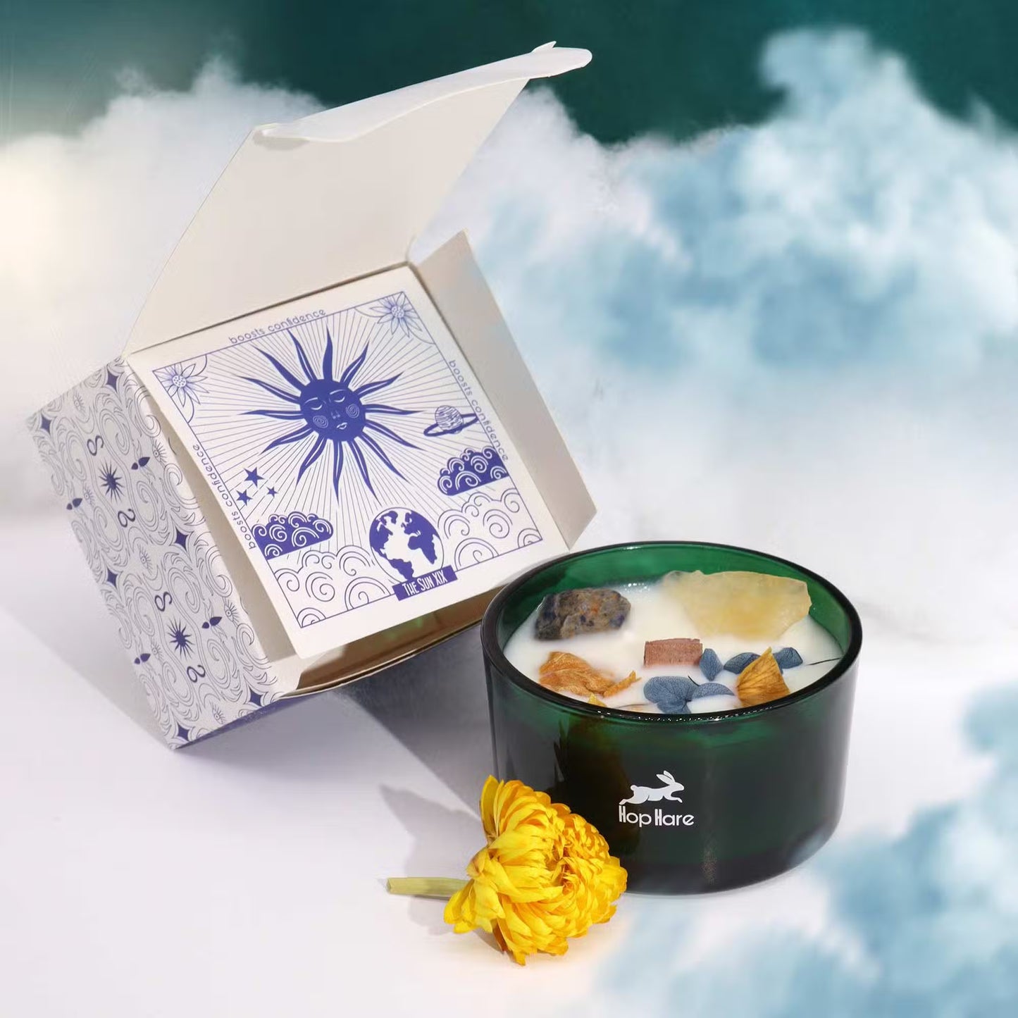 'The Sun.' Candle with crystals and dried flowers in a green glass jar. Next to a decorative gift box and yellow flower. 
