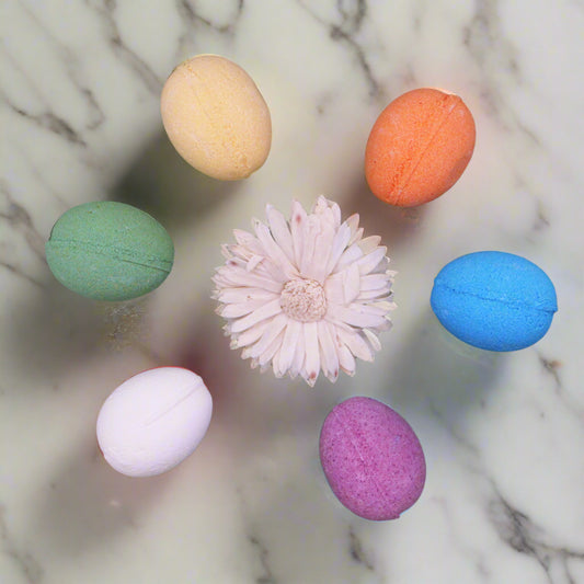 Egg shaped bath bombs in six colours on a marble worktop with a white flower in the centre.