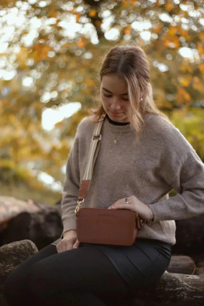 Woman sitting outside. Holding a Bayraw brown leather crossbody bag. 
