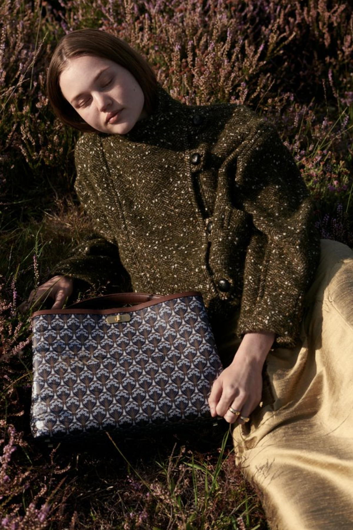 Woman laid down outdoors on heather. A Liberty Burlington bag is at her side.