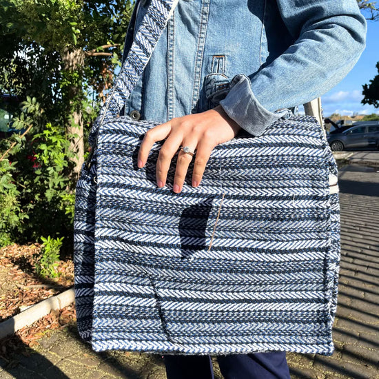 Close up of a woman carrying a cotton laptop bag outdoors. It has horizontal blue and grey stripes.