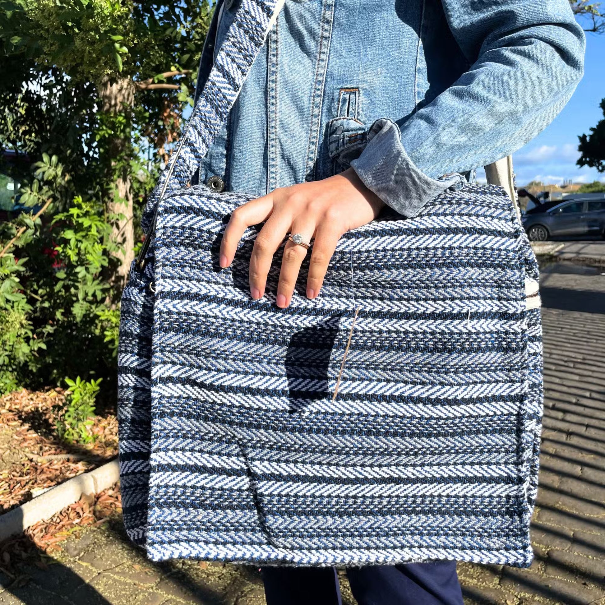 Close up of a woman carrying a cotton laptop bag outdoors. It has horizontal blue and grey stripes.